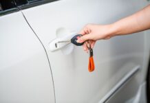 Kluczyk w smartfonie: czy cyfrowy dostęp do auta jest naprawdę bezpieczny dla właścicieli supersamochodów Dłoń otwierająca drzwi białego auta kluczykiem i pilotem