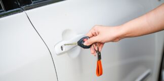 Kluczyk w smartfonie: czy cyfrowy dostęp do auta jest naprawdę bezpieczny dla właścicieli supersamochodów Dłoń otwierająca drzwi białego auta kluczykiem i pilotem