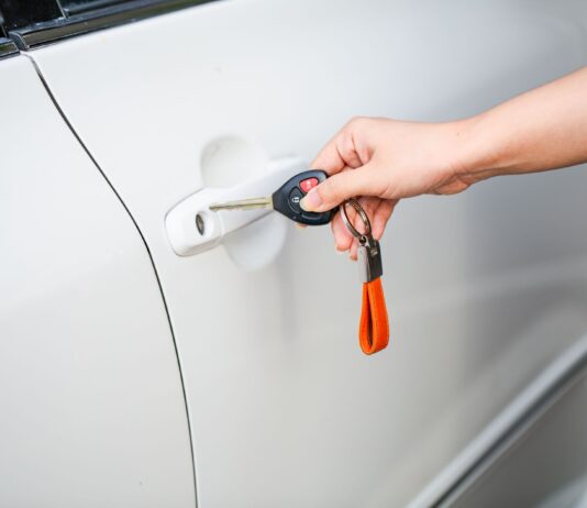 Kluczyk w smartfonie: czy cyfrowy dostęp do auta jest naprawdę bezpieczny dla właścicieli supersamochodów Dłoń otwierająca drzwi białego auta kluczykiem i pilotem